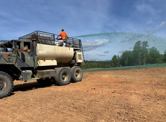 Hydroseeding truck spraying seed mixture across a graded site